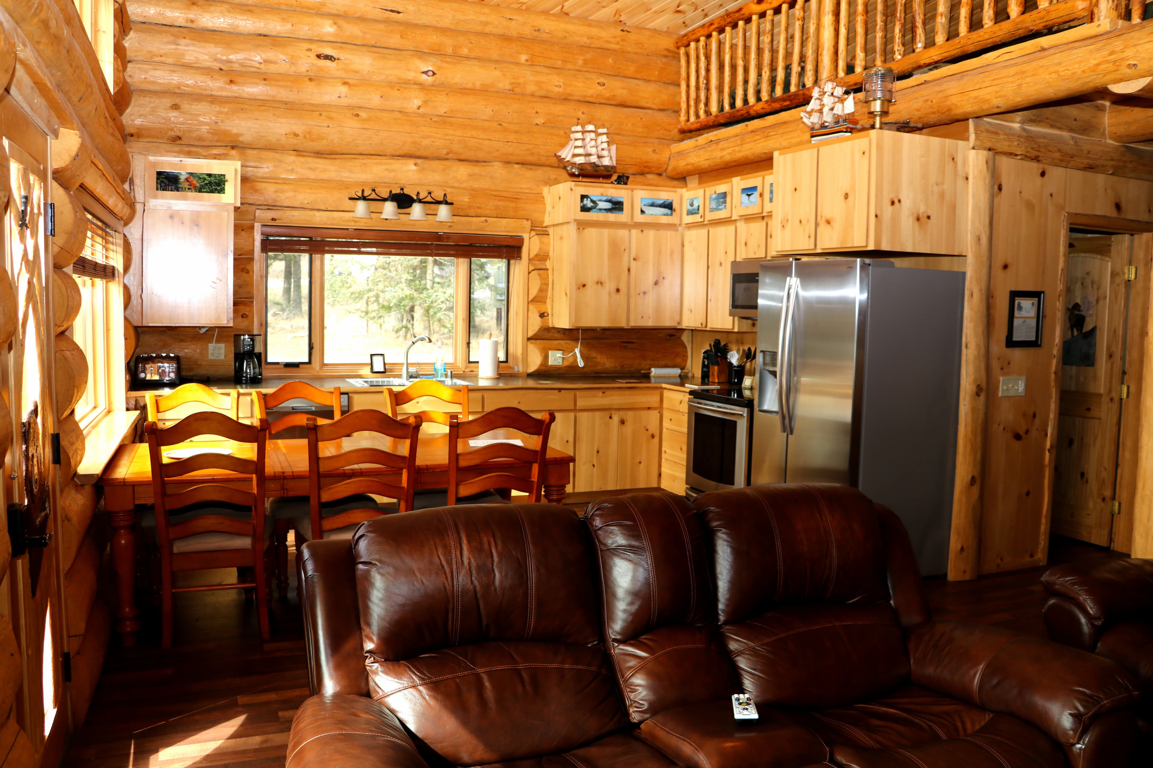 First Floor View 1 with dining area and kitchen in the background and brown leather couch in the foreground.
