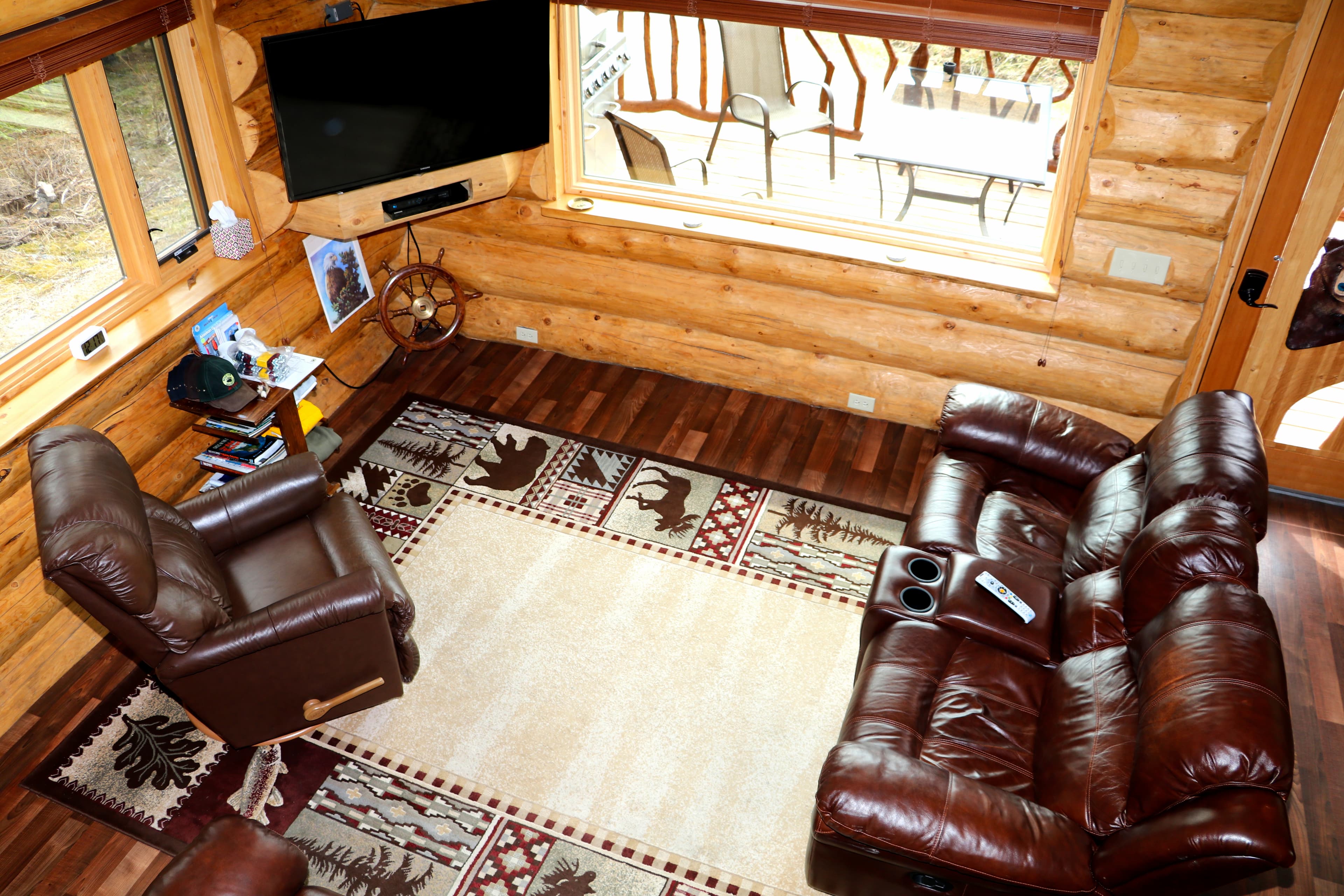 View of den from loft shows rich brown loveseat and recliner in sunlit room with TV.