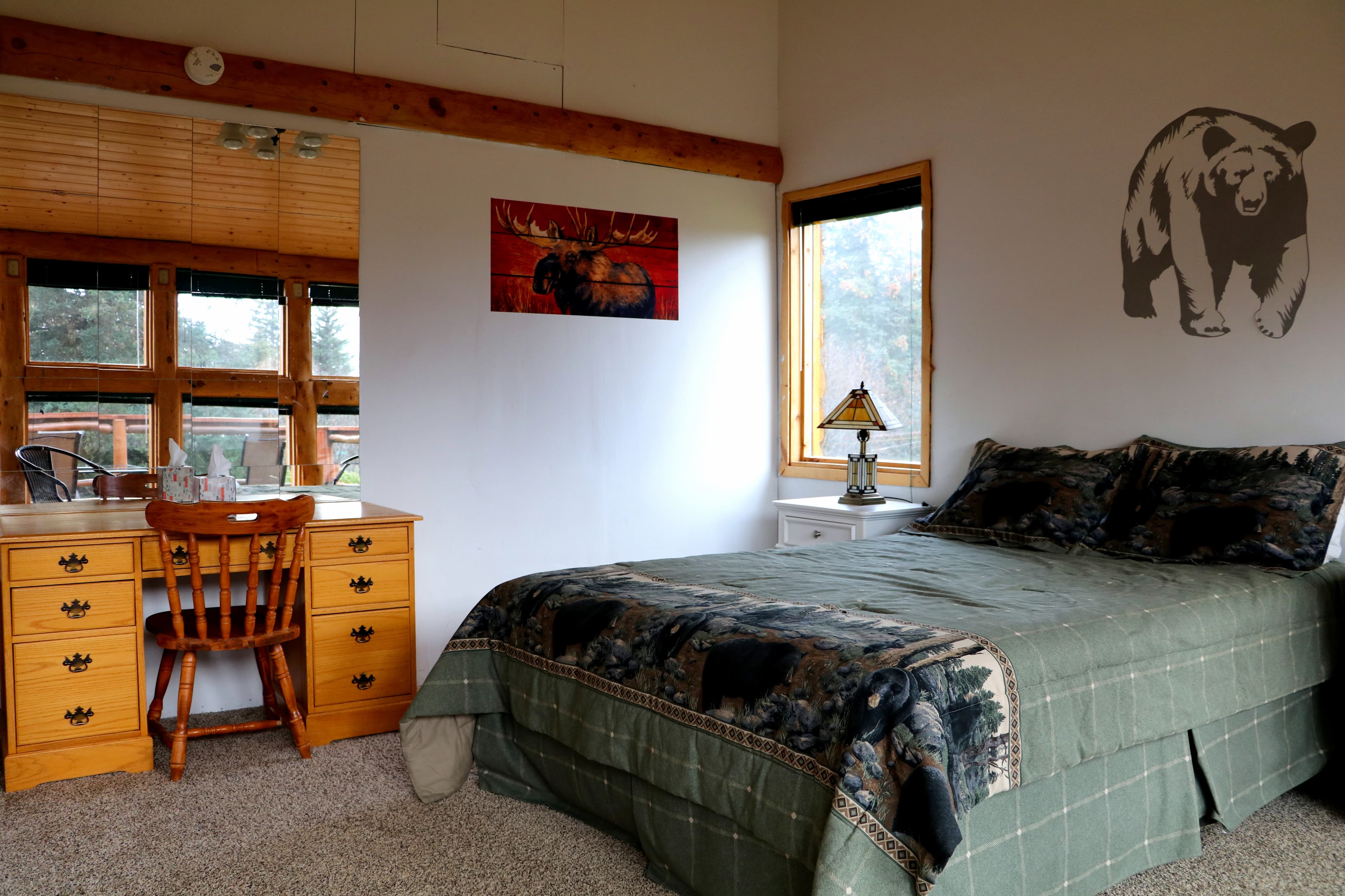 Queen Bedroom with wooden desk and chair, window with view of deck, nightstand with table, and silhouette of bear on wall over bed.