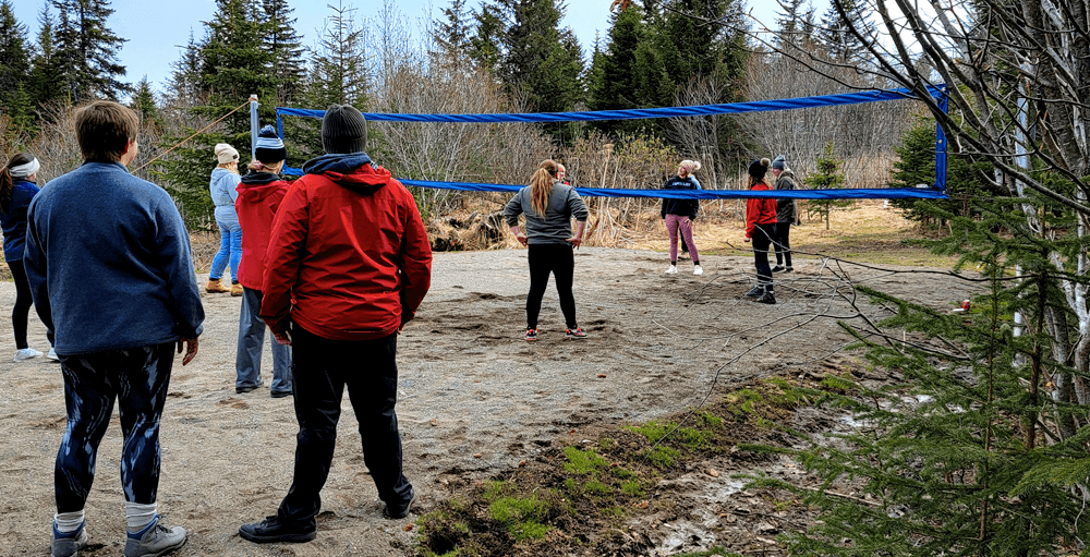 A group of people is playing beach volleyball in a forested area.