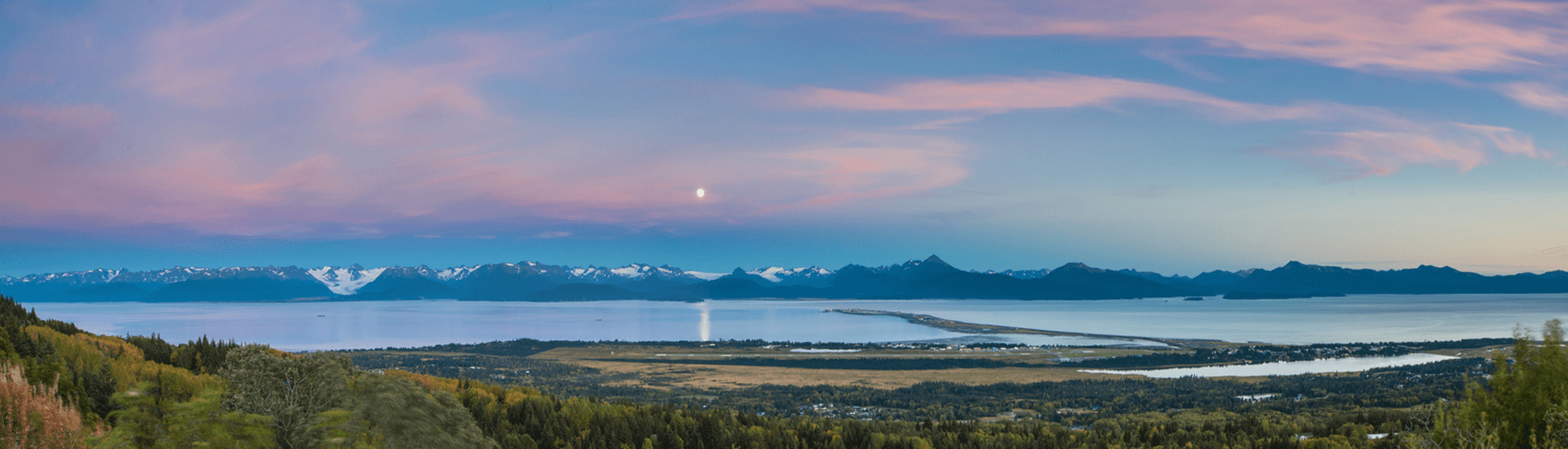 A panoramic view of a tranquil landscape at dusk, featuring mountains, a serene body of water, and colorful skies.