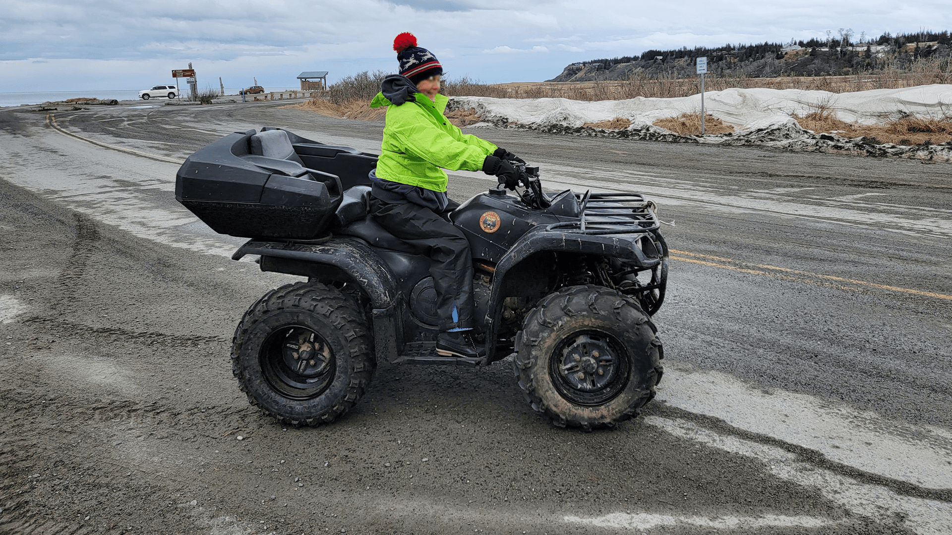 A person in a bright jacket rides an all-terrain vehicle on a gravel road.